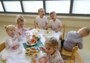 dzieci siedzą przy stole i jedzą śniadanie wielkanocne