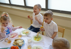 dzieci siedzą przy stole i jedzą śniadanie wielkanocne