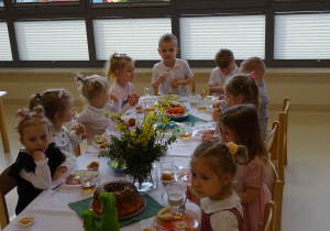 dzieci siedzą przy stole i jedzą śniadanie wielkanocne