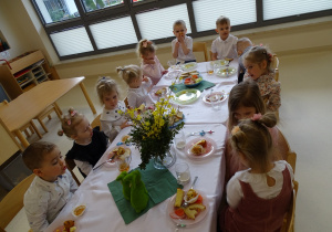 dzieci siedzą przy stole i jedzą śniadanie wielkanocne