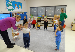 Dzieci wykonują ćwiczenia oddechowe, logopeda pomaga chłopcu wykonać ćwiczenie