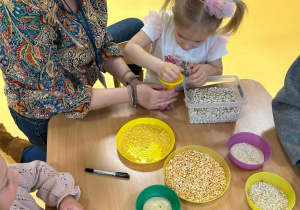 Logopedka przyrzymuje lejek dziewczynce podczas wypełniania balonika grochem