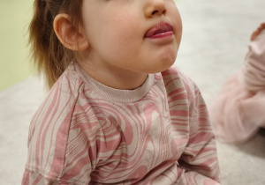 Dziewczynka zasłania językiem czerwień wargi górnej