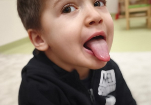 Chłopiec wystawia język w ćwiczeniu o nazwie Wąż