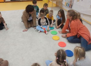 Chłopiec dotyka sensorycznych krążków, dzieci z nauczycielkami obserwują