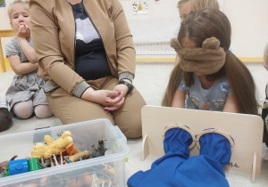 15. Kolejna dziewczynka dotyka zabawki schowanej w niebieskim woreczku, obok siedzi nauczycielka