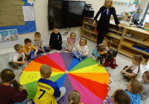 Dzieci podczas zabawy z chustą, owocami i literami.