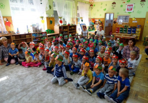 Dzieci siedzą na dywanie w kolorowych opaskach na głowie