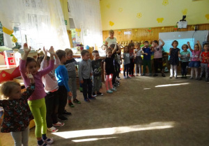 Dzieci z uniesionymi do góry rękami śpiewają piosenkę