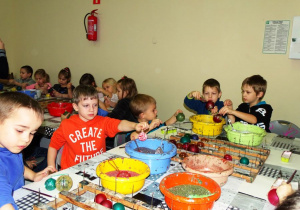 Dzieci siedzą przy stole i dekorują bombki
