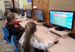 Dzieci siedzą przed komputerami na zajęciach informatycznych