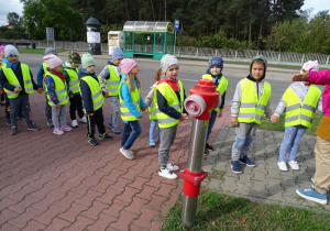 Dzieci oglądają hydrant oraz przystanek autobusowy.