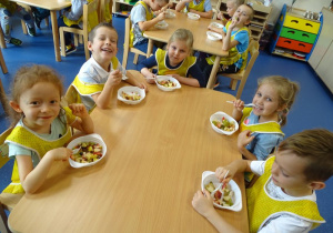 Dzieci spożywają przygotowaną przez siebie sałatkę owocową.
