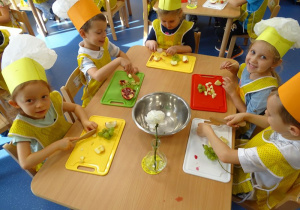 Dzieci przygotowują sałatkę owocową.