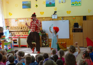 Dziewczynka w peruce stoi na scenie z klaunem i trzyma kółko