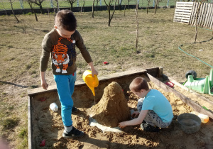 Szymon i Daniel budują w piaskownicy wulkan.