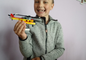 Uśmiechnięty Szymuś trzyma w ręku helikopter z klocków LEGO