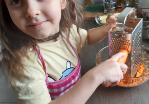 Karolcia ściera marchewkę na tarce.