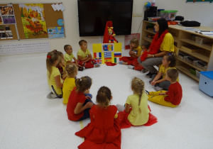 Dzieci w żółto-czerwonych strojach siedzą w kole.