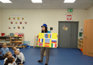 Nauczycielka pokazuje dzieciom plakat z flagami.