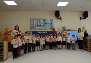 Dzieci ubrane na galowo trzymają flagi Polski